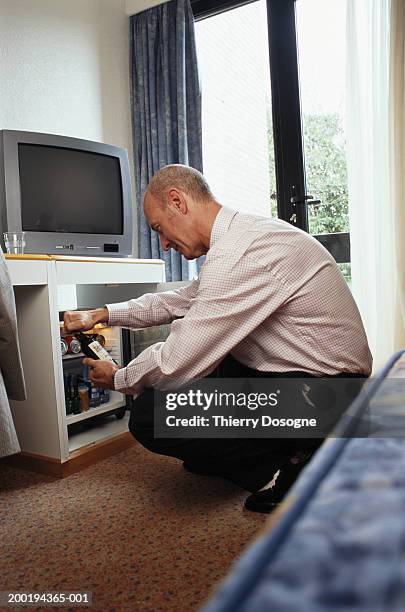 businessman selecting bottle from hotel room mini bar - mini bar imagens e fotografias de stock