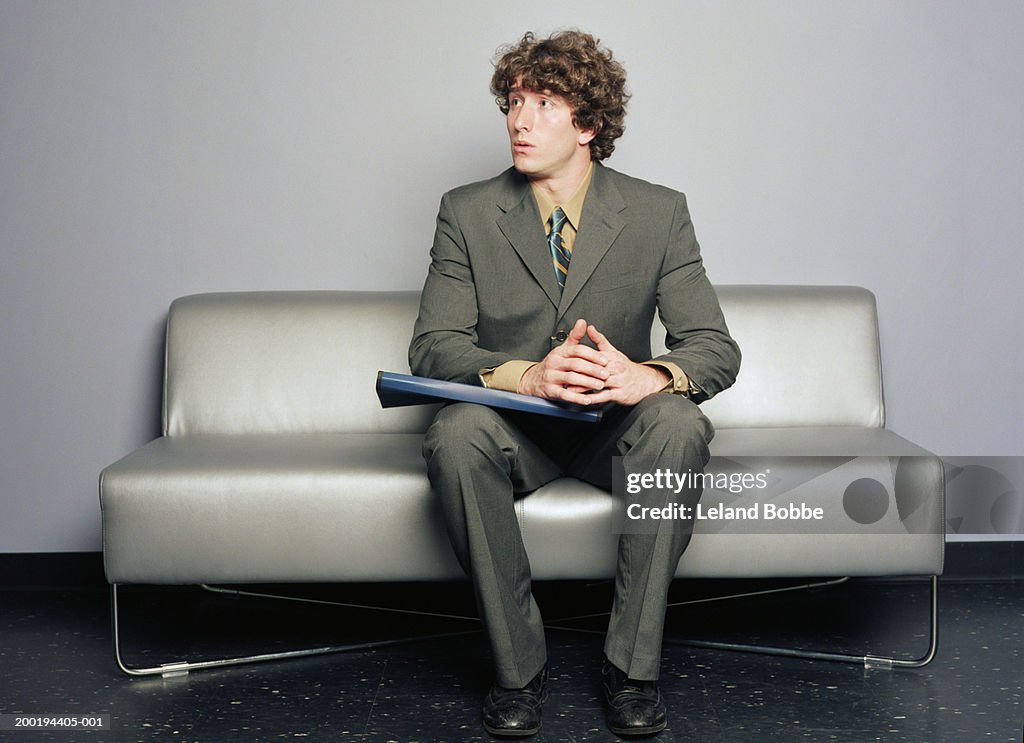 Young man sitting on sofa, looking off to side