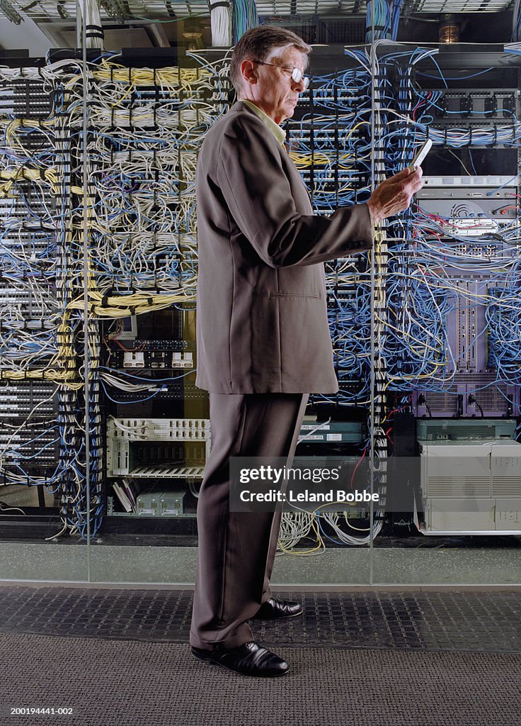 Mature businessman looking at mobile phone near server, side view
