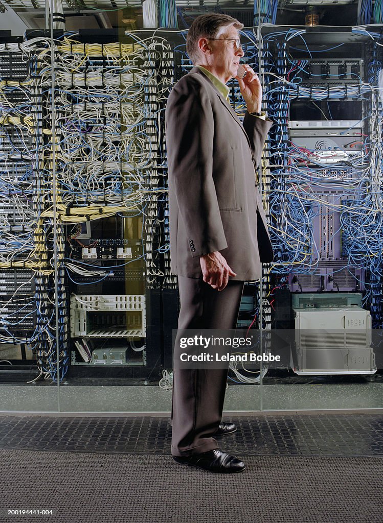 Mature businessman using mobile phone near server, side view