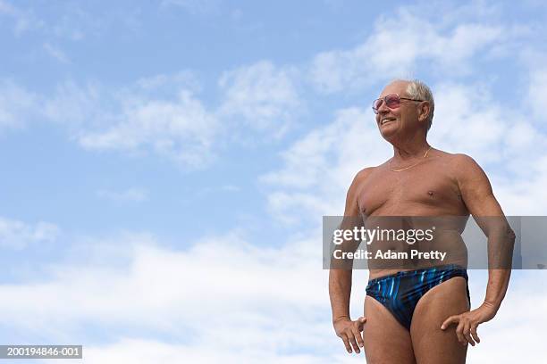 senior man wearing swimming trunks and rose-tinted sunglasses, smiling - zwembroek stockfoto's en -beelden