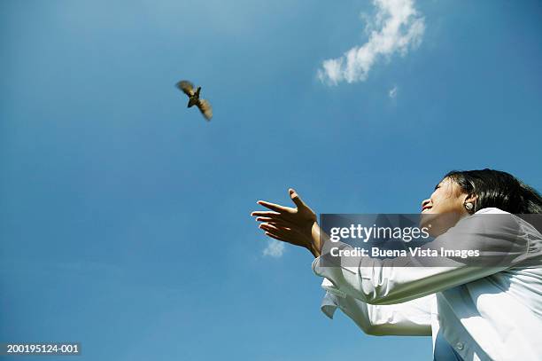 young woman releasing bird smiling, low angle view - releasing fotografías e imágenes de stock