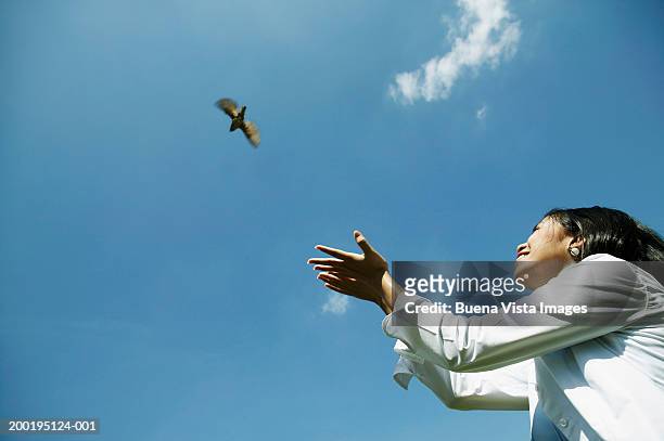 young woman releasing bird smiling, low angle view - releasing stock pictures, royalty-free photos & images
