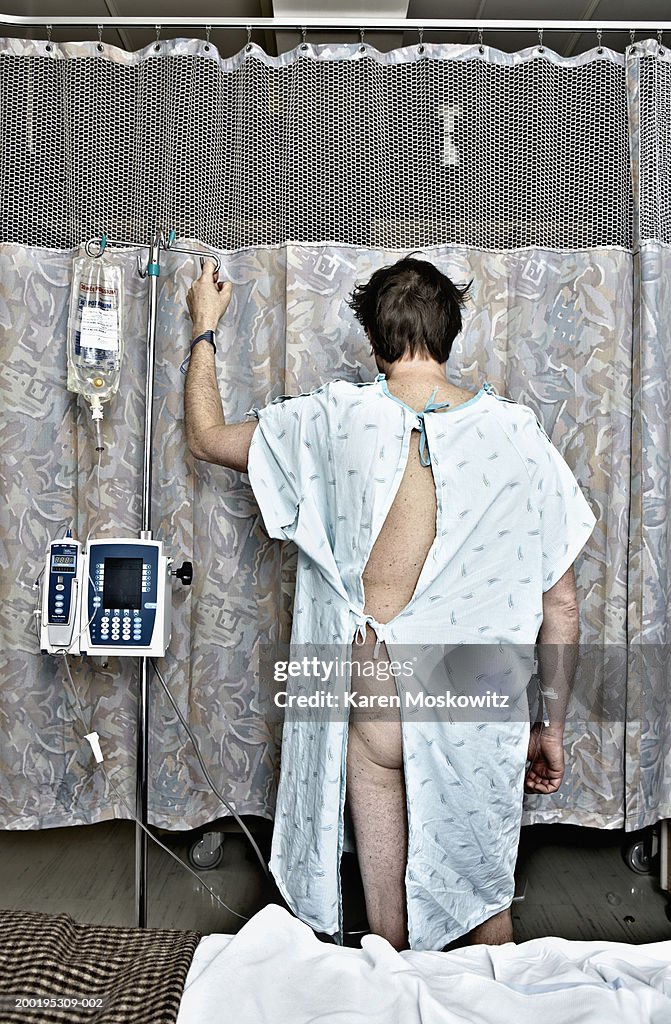 Mature man in examination gown with IV drip, rear view