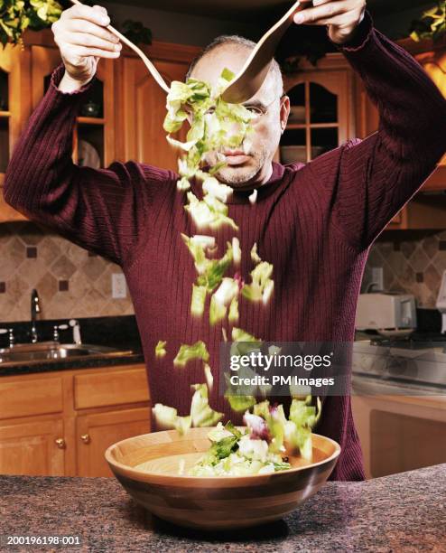 mature man tossing salad in kitchen - salad server stock pictures, royalty-free photos & images