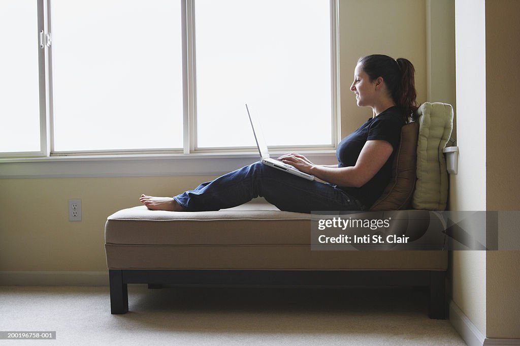 Woman sitting on couch, using laptop, side view