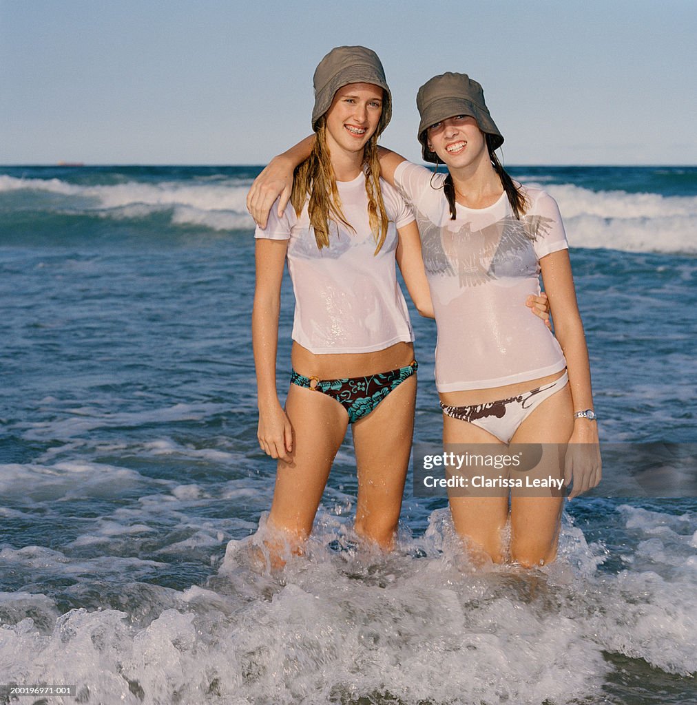 Two girls (15-17) standing together in surf, portrait