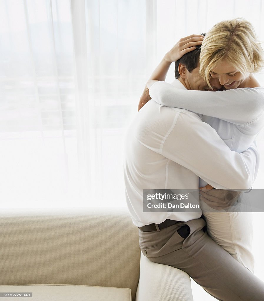 Young couple embracing on arm of sofa, smiling, side view