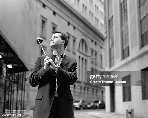 businessman with golf club on shoulder in street (b&w) - golf short iron stock pictures, royalty-free photos & images