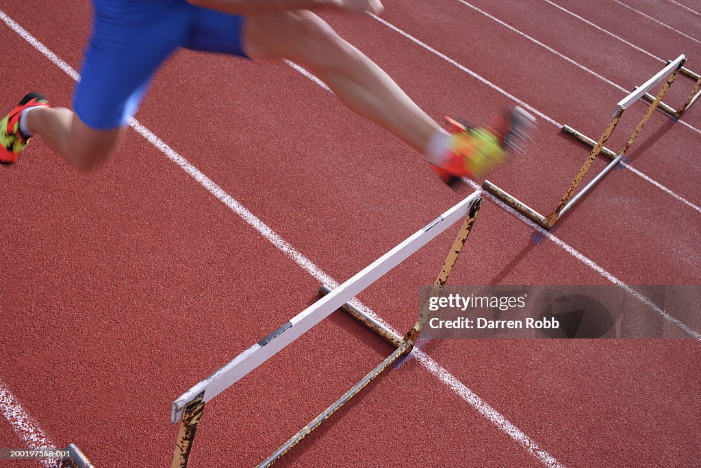 Male athlete jumping hurdle, low section (blurred motion)