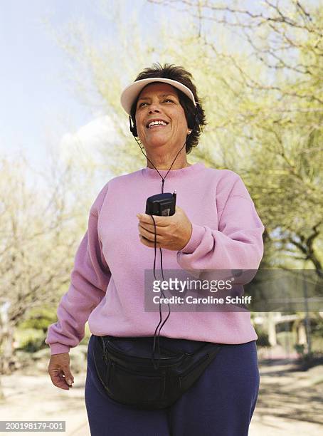 senior woman wearing headphones, exercising in park, smiling - sun visor stock pictures, royalty-free photos & images