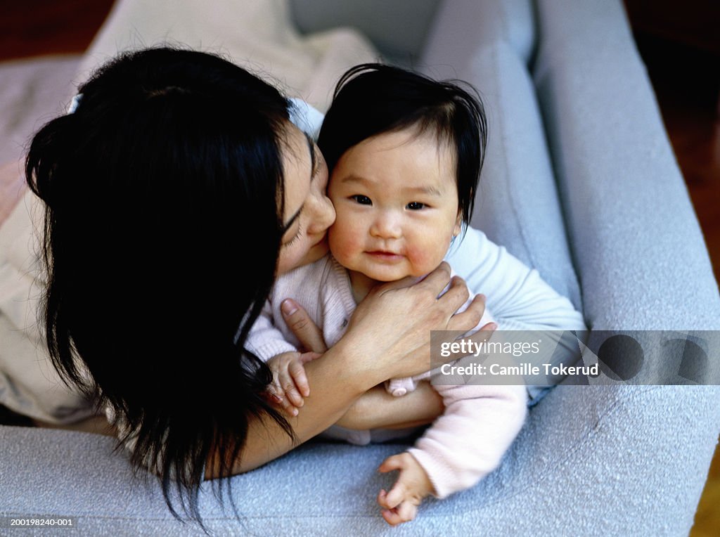 Mother kissing baby daughter (6-9 months) on couch, portrait, close-up