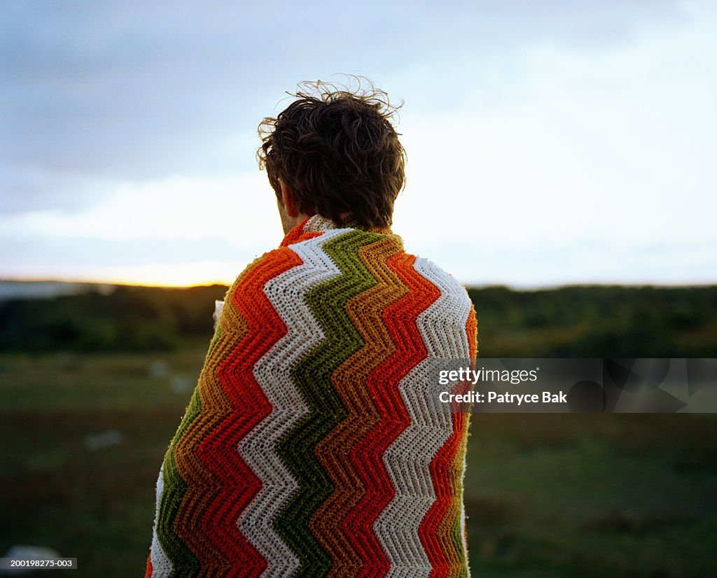 Young man wrapped in blanket, rear view