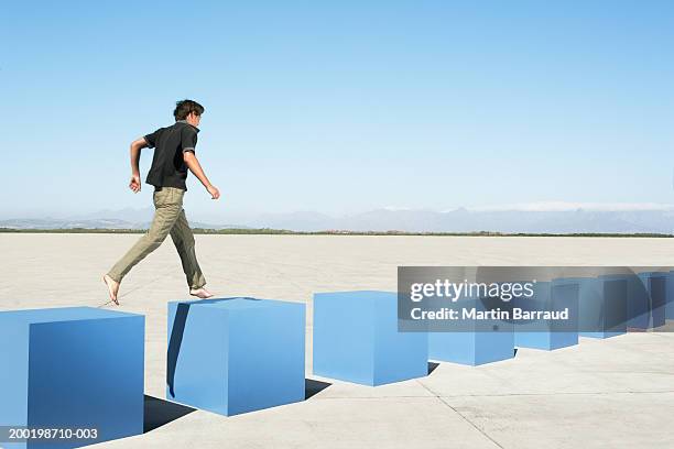 young man walking on row of large cubes in barren landscape - next steps stock-fotos und bilder