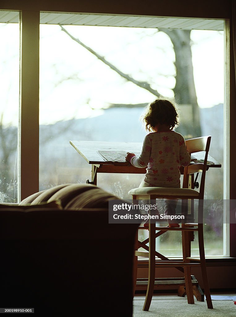 Girl (3-5) at drawing table near living room window, rear view