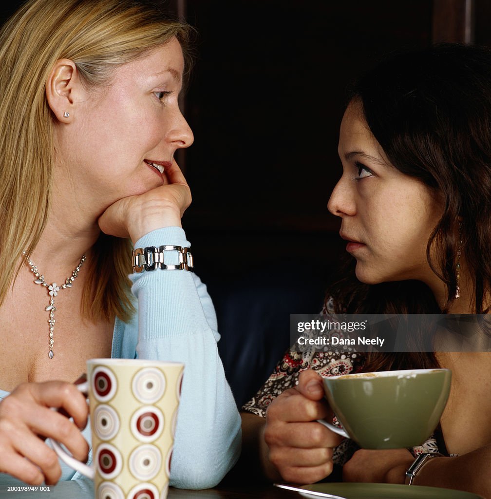 Two women holding drinks, looking at each other, close-up