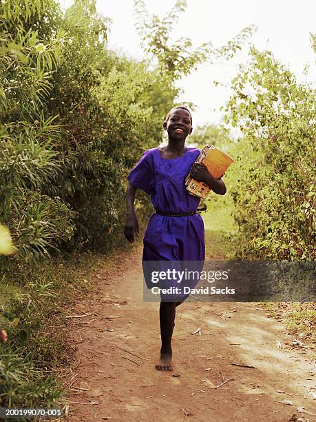 girl (8-10) holding books, and running, smiling - uganda stock-fotos und bilder