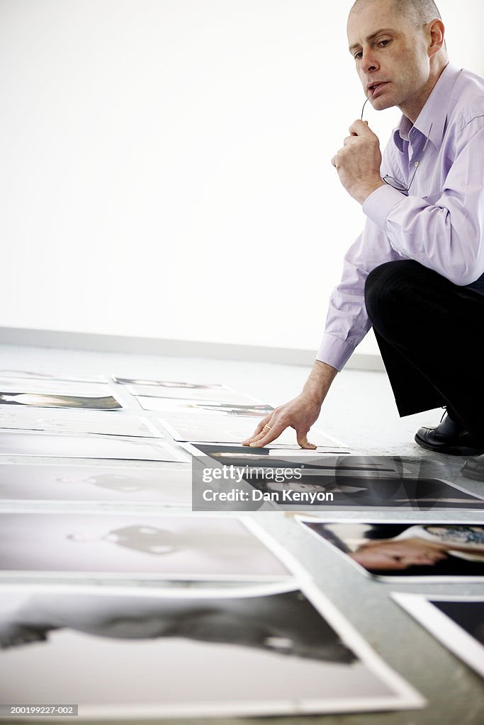 Mature man crouching by images laid out on floor