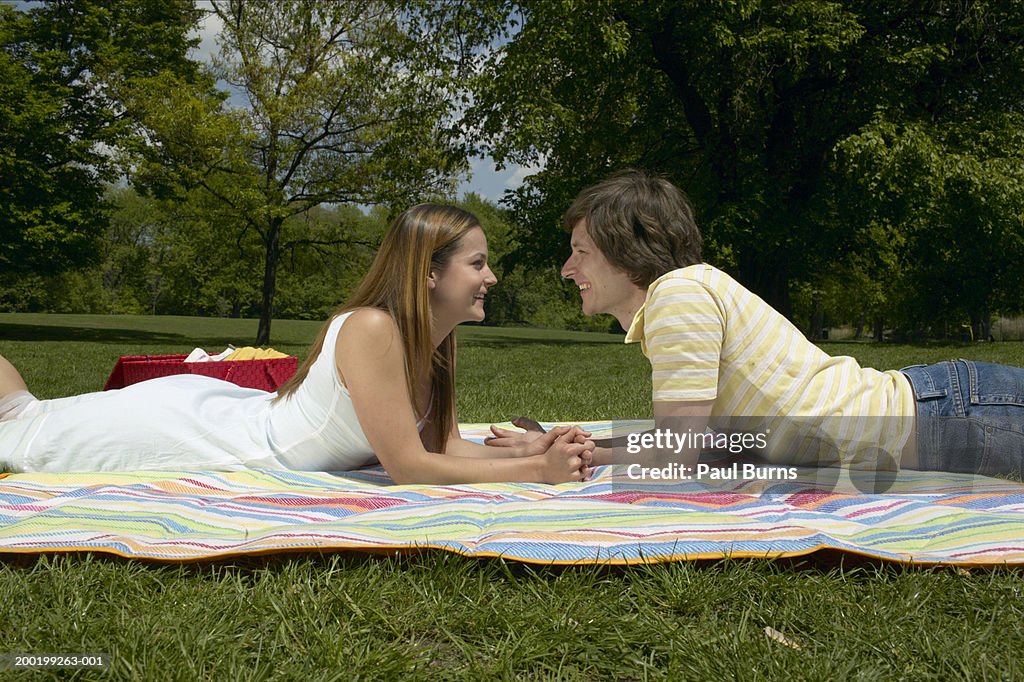 Young couple in park, lying face to face on blanket, smiling, profile