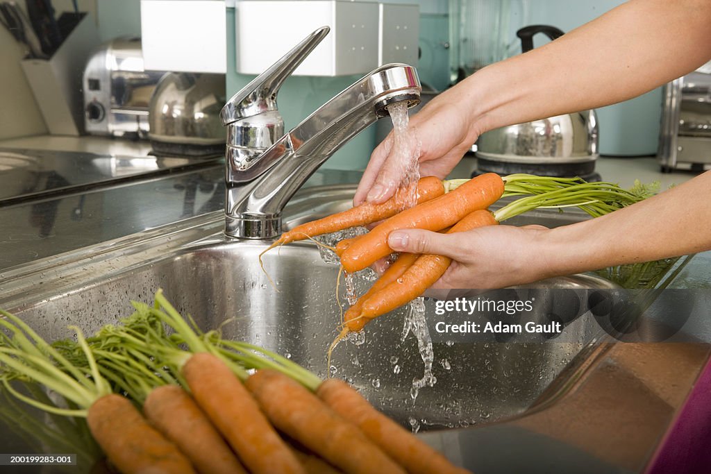 Woman washing carrots at kitchen sink, close-up