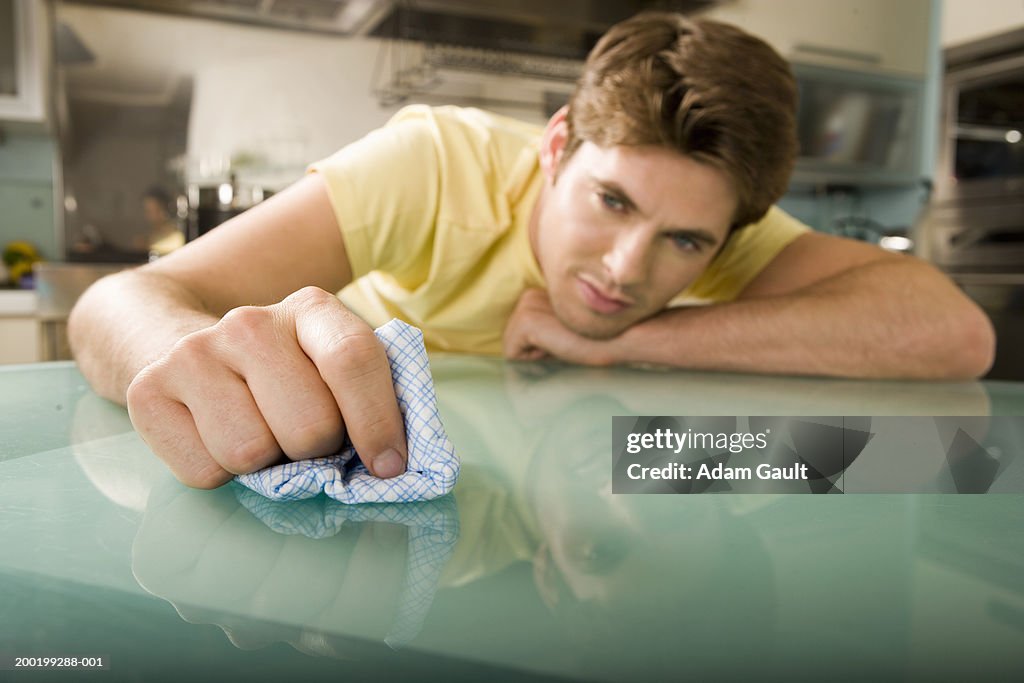 Young man wiping glass table with cloth