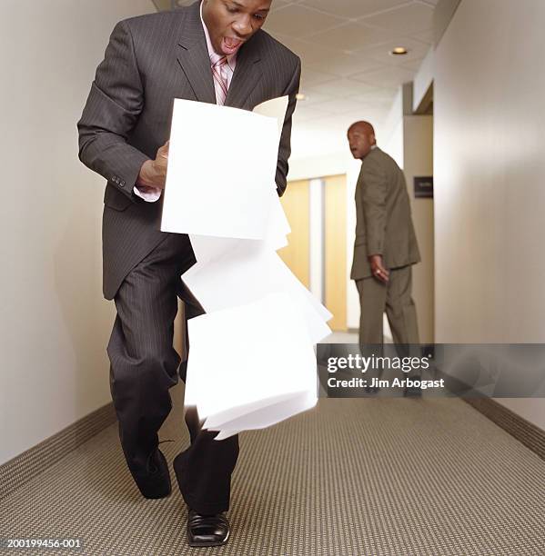 two businessmen in corridor, one man dropping stack of documents - inciampare foto e immagini stock
