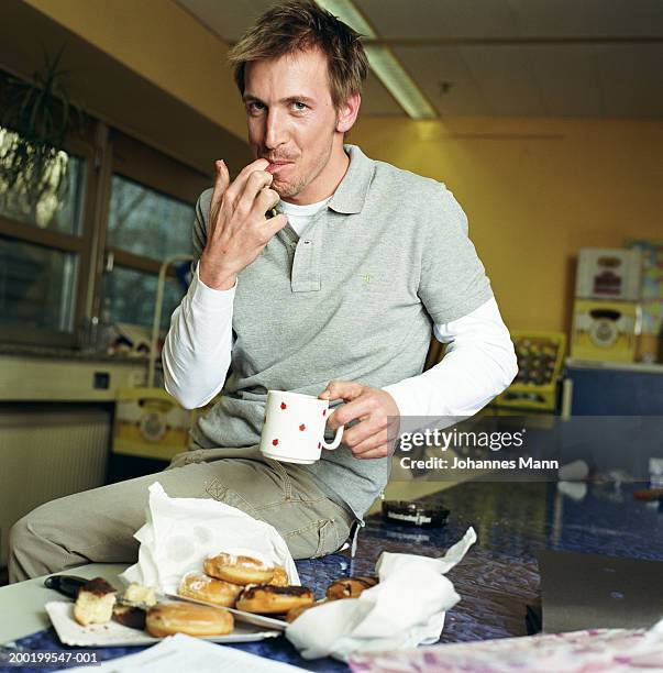 man in kitchen by doughnuts, licking fingers, portrait - 指をくわえる ストックフォトと画像