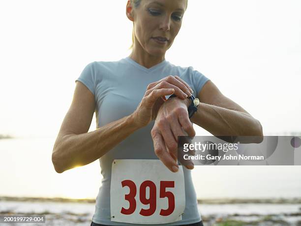 woman wearing race number looking at watch, close-up - sports bib stock pictures, royalty-free photos & images