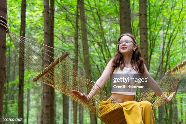 summer bliss - teenage girl in eyeglasses swinging in hammock amidst coniferous forest - hammock stock pictures, royalty-free photos & images