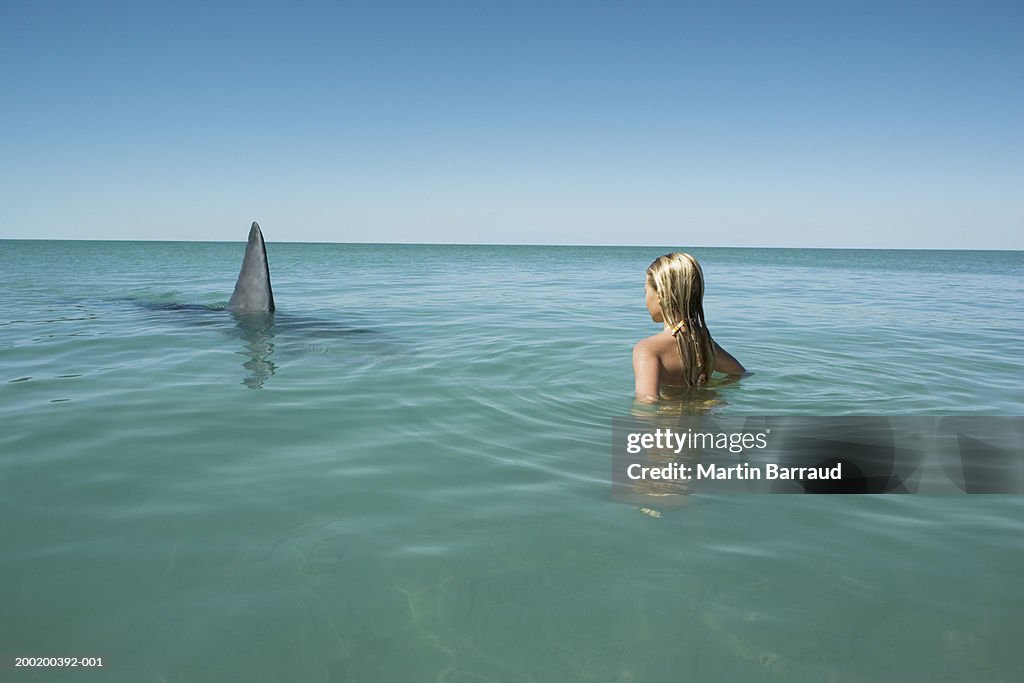 Girl (8-10) facing Great white shark, fin breaking surface of sea