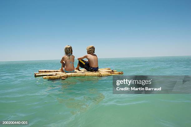 girl (6-8) and boy (10-12) sitting on bamboo raft in sea, rear view - floß stock-fotos und bilder