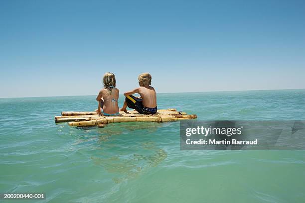 girl (6-8) and boy (10-12) sitting on bamboo raft in sea, rear view - bamboo raft ストックフォトと画像