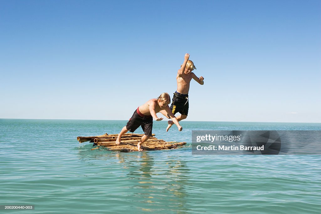 Two boys (10-12) jumping into sea from bamboo raft