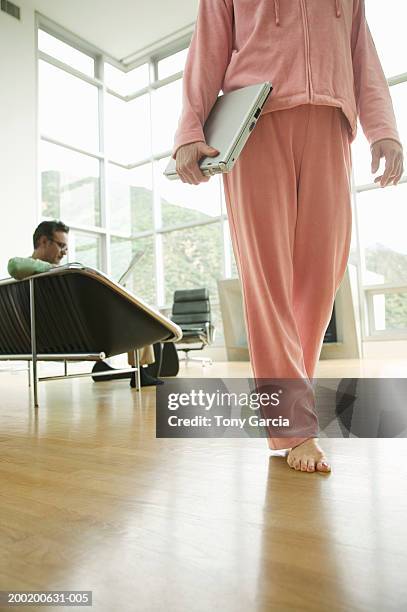 woman walking in house with laptop, man reading paper in background - track suit stock pictures, royalty-free photos & images