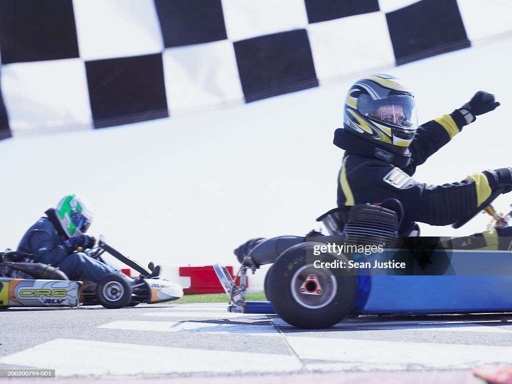 Go-cart racer crossing finish line, raising arm, side view