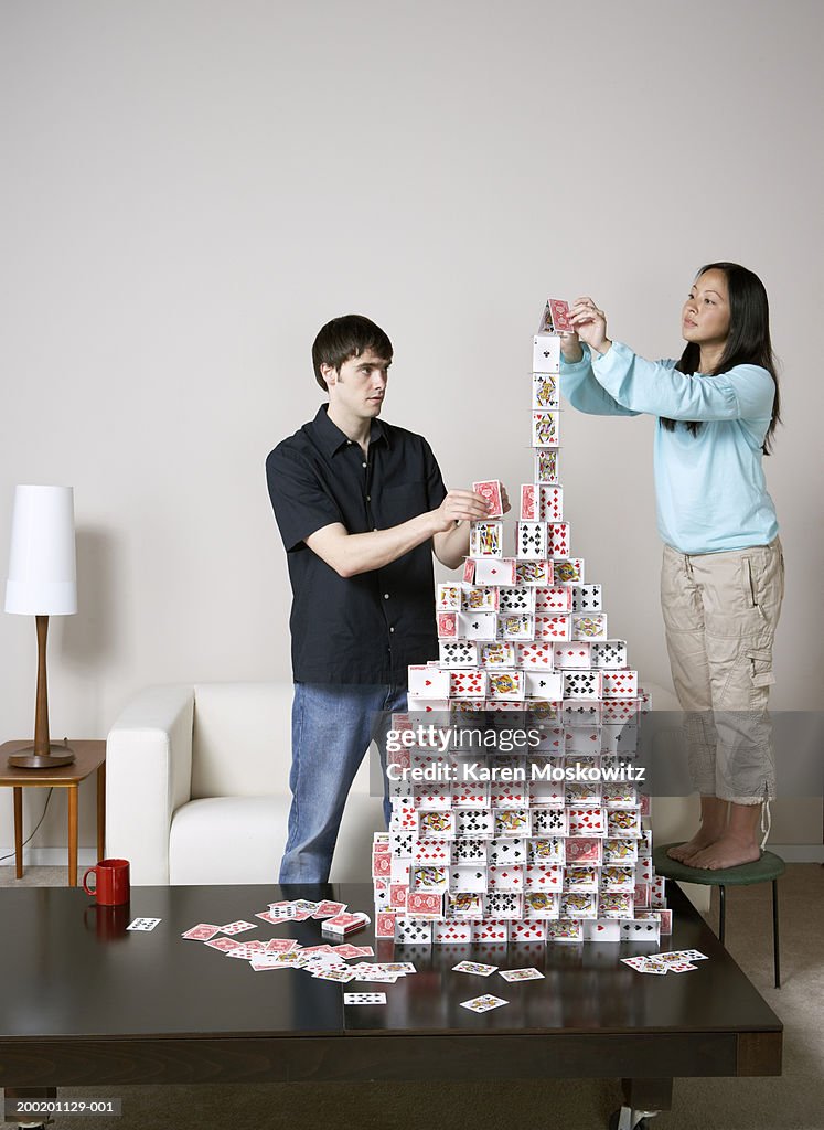 Young man and woman building house of cards on coffee table