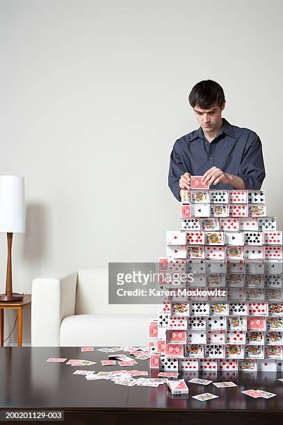 young man building house of cards on coffee table - card house stock pictures, royalty-free photos & images