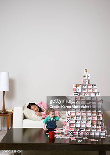 baby boy (9-12 months) touching house of cards, woman sleeping on sofa - child prodigy stockfoto's en -beelden