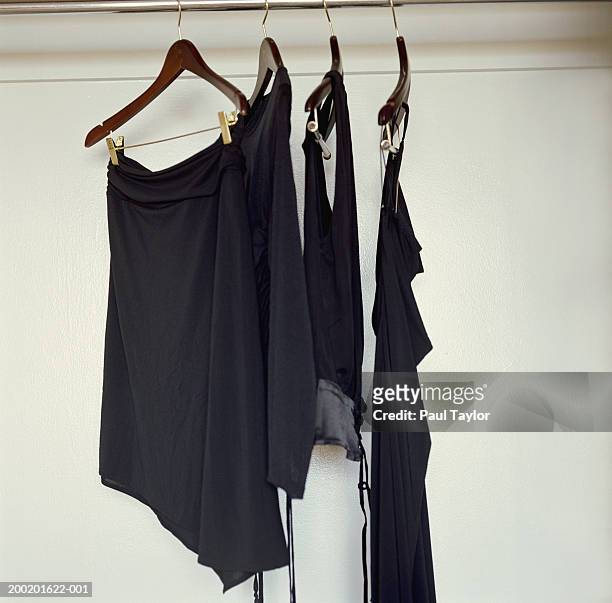 black clothing hanging from hangers in closet - black skirt stock-fotos und bilder