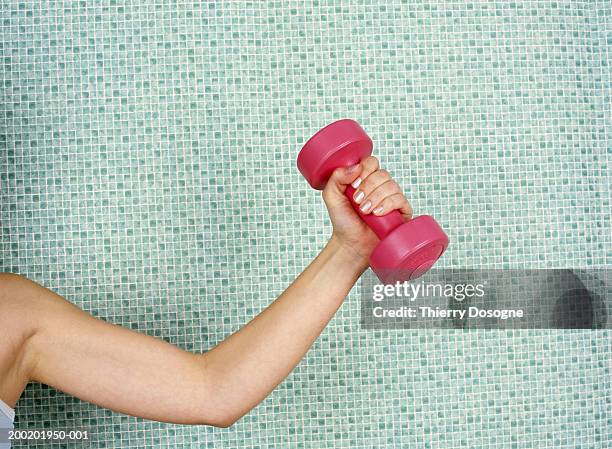 young woman lifting dumbbell, against tiled wall, close-up - mancuerna fotografías e imágenes de stock