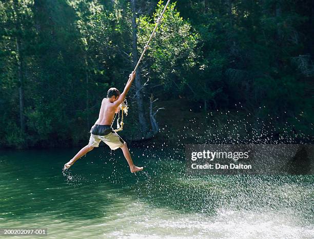 teenage boy (13-15) swinging on rope over lake, rear view - altalena di corda foto e immagini stock