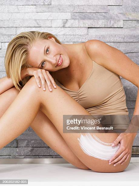 young woman applying cream to leg, resting head on knee, portrait - body lotion stock-fotos und bilder