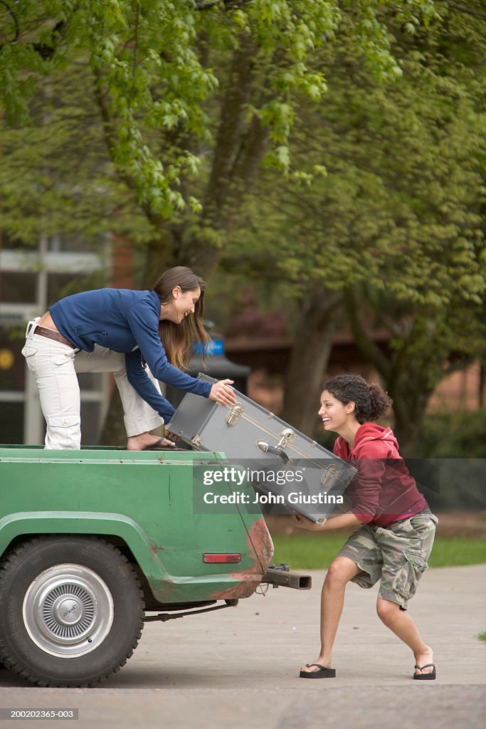 Two female students lifting trunk onto truck, side view