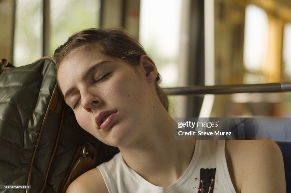 Young woman resting head against luggage, eyes closed, close-up