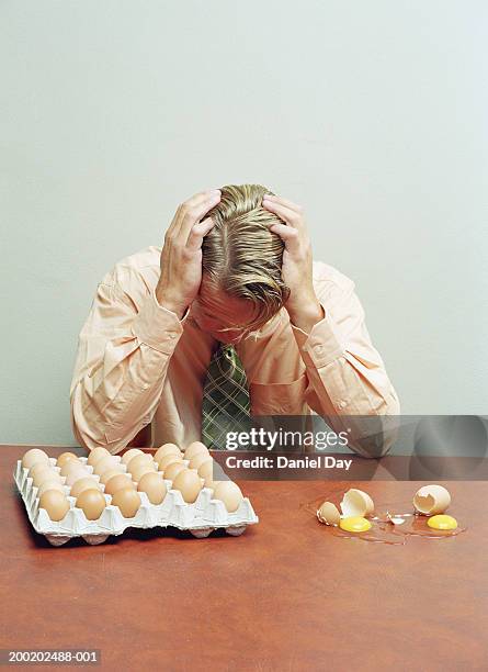 man sitting at table with two eggs cracked open, holding head in hands - äggkartong bildbanksfoton och bilder