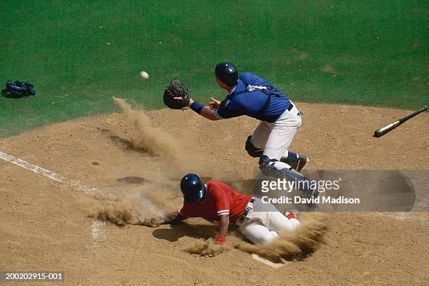 baseball catcher fielding ball as base runner slides into home - baseball fields stock-fotos und bilder