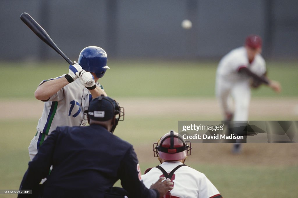 Baseball pitcher pitching ball toward batter, catcher and umpire