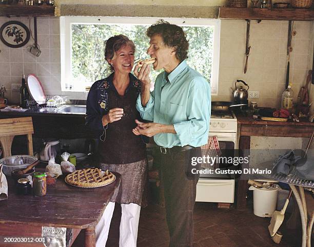 mature couple in kitchen, man eating wedge of pie - middle aged couple cooking stock-fotos und bilder