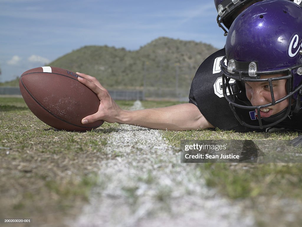 Teenage boy (16-18) football player on field, touching ball
