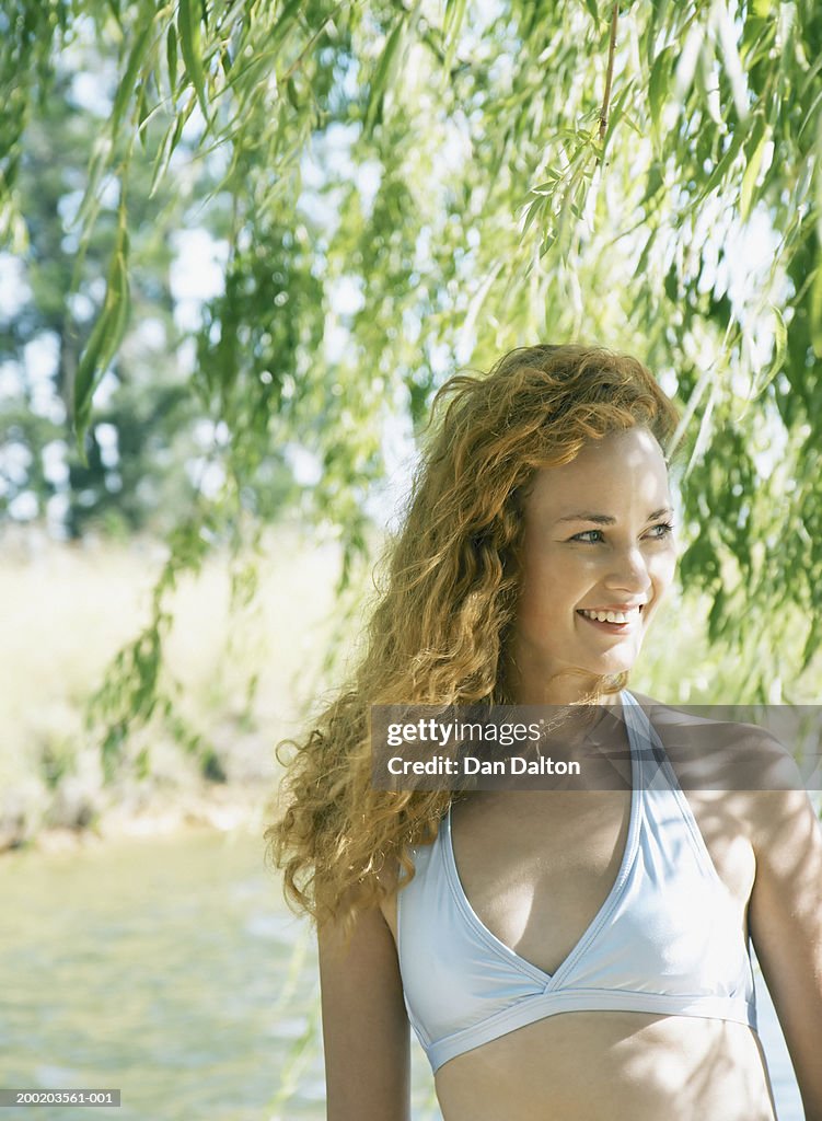 Young woman standing under willow tree, smiling